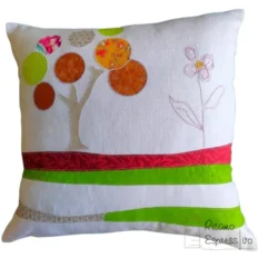 Cuscino artigianale in cotone e lino su cui si ha un albero in applique che sorge su un terreno stratificato da vari tessuti e da un fiore ricamato a mano.