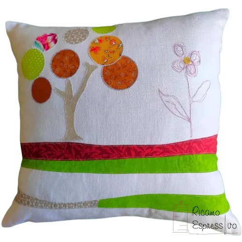Cuscino artigianale in cotone e lino su cui si ha un albero in applique che sorge su un terreno stratificato da vari tessuti e da un fiore ricamato a mano.