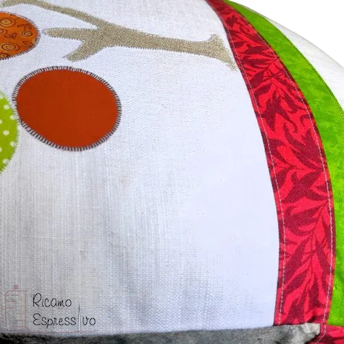 Cuscino artigianale in cotone e lino su cui si ha un albero in applique che sorge su un terreno stratificato da vari tessuti e da un fiore ricamato a mano.